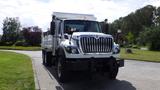 A white 2014 International 7500 truck with a large front grill and a flatbed is parked on a paved surface with greenery in the background