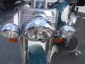 A close-up view of the front chrome headlight assembly of a 2009 Harley-Davidson Flstc featuring three round headlights and an orange indicator light