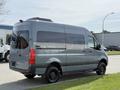 A gray 2019 Mercedes-Benz Sprinter van with a high roof and large windows is parked on a grassy area with visible wheels and side detailing