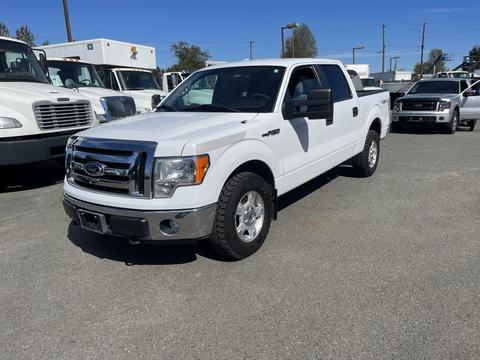 A white 2012 Ford F-150 truck with a chrome grille and alloy wheels parked on a gravel surface