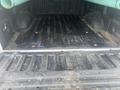 A 2013 Ford F-150 truck bed showing a dirty and scratched black bed liner with some debris and two green pipes resting in the back