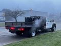 A 2015 Ford F-550 truck with a flatbed and a black storage unit on the back emitting steam from a hood vent