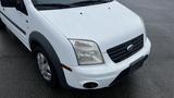 A white 2012 Ford Transit with a distinctive front grille and headlights is shown from a close angle focused on the front end of the vehicle