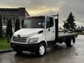 A 2006 Hino 155 flatbed truck with a white cab and black flatbed, featuring a two-door design and prominent front grille with the Hino logo