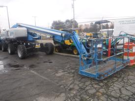 A 2018 Genie S-65 aerial lift with a blue platform and arm extended for high access work sitting on a paved surface