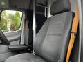 Interior view of a 2016 Mercedes-Benz Sprinter showing the driver's seat with a grey fabric cover and an orange seatbelt