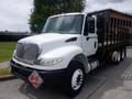 A white 2015 International 4400 truck with a flatbed and wooden side panels, featuring a prominent front grille and several orange marker lights on the roof