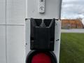 A close-up of a black mounting bracket with a metal bolt on a white surface next to a red circular light on a 2006 Hino 268 truck