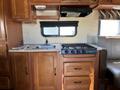 Interior of a 2012 Ford Econoline showing a kitchenette with a sink a gas stove and wooden cabinetry