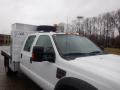 A white 2009 Ford F-450 SD with a flatbed and a storage box on the back featuring an additional tire on the roof and amber lights on the cab