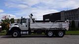 A 2014 International 7500 dump truck with a white body and black bed is parked on the street with a hydraulic arm extended from the bed