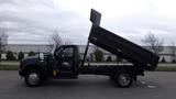 A 2008 Ford F-450 SD with its dump bed raised, showcasing a dark exterior and a single cab design, positioned for unloading materials