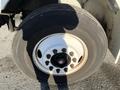 A close-up of a large truck tire mounted on a white wheel with multiple bolts visible in the center and a worn tread on the rubber surface