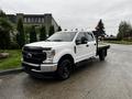 A white 2020 Ford F-350 SD with a flatbed, featuring a black front grille and hood, parked on a gravel surface