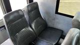 Two black leather seats in a bus interior with a smooth gray panel behind them