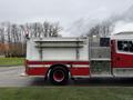 A red and white 2001 Freightliner FL80 fire truck with a storage compartment and equipment mounted on the side