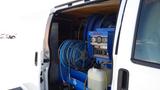 A 2012 GMC Savana van with a blue cleaning machine and several coiled hoses stored inside