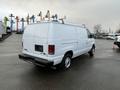 A white 2013 Ford Econoline van with a ladder rack on the roof and chrome wheels viewed from the rear angle