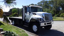 A white 2015 International 7400 flatbed truck with a black bed and shiny chrome front grille parked on a concrete surface