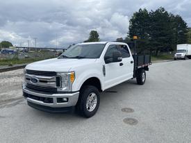 A white 2017 Ford F-350 Super Duty pickup truck with a flatbed and side toolboxes parked on a road