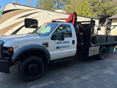 A 2008 Ford F-550 pickup truck with a flatbed and crane attachment in a white and black color scheme