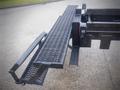 A black metal loading ramp attached to a 2006 International 4300 truck with a perforated surface for traction