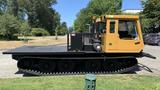 A 2015 PowerBully Tracked Flat Deck Equipment Carrier with a yellow cab and black flat deck featuring a tracked undercarriage for movement over rough terrain