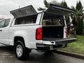 A white 2019 Chevrolet Colorado with an open bed and a canopy featuring lifted doors, revealing the cargo area with a black rubber mat