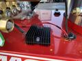 A close-up of a black heat sink with two wires attached on a red surface near various pressure washer components