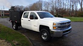 A white 2016 Chevrolet Silverado 3500HD with a flatbed and chrome accents parked at an angle showcasing its front and side view