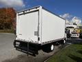 A 2016 Isuzu NPR box truck with a white cargo area and a black lower section parked with an empty trailer hitch visible