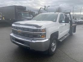 A 2015 Chevrolet Silverado 3500HD pickup truck in white with chrome accents and a flatbed design parked prominently in the foreground