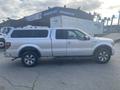 A 2014 Ford F-150 pickup truck in white with a cap over the bed and alloy wheels parked on a lot