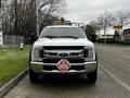 A 2018 Ford F-550 truck with a white exterior featuring a front grille and a warning light on top along with a hazard placard attached to the front bumper