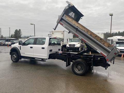 A white 2021 Ford F-550 dump truck with its bed raised, showcasing a wooden loading area and a side view of the cab and chassis