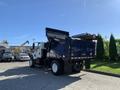 A 2007 International 7300 dump truck with a blue cargo bed tilted for unloading and equipped with tools and equipment on the back