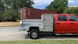 A red 2013 RAM 2500 with a silver utility bed and chrome wheels parked next to a shipping container