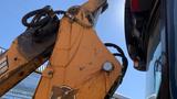 Close-up of the arm and bucket of a 2015 Case 580 backhoe loader with hydraulic hoses and markings visible on the yellow metal surface