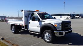 A white 2016 Ford F-550 truck with a flatbed and an orange light on top parked in a lot