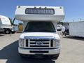 A white 2012 Ford Econoline with a large overhead camper shell in the front, showing a chrome grille and headlights