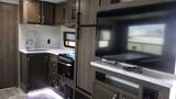 Interior view of a 2021 Forest River 312BH East To West Della Terra showing a kitchen area with a sink stove and a television mounted on a cabinet