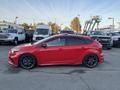 A red 2018 Ford Focus hatchback with black wheels and a sporty design is parked alongside other vehicles