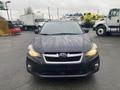 A black 2014 Subaru Impreza facing forward with headlights on and a wet windshield