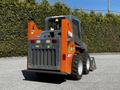 A 2017 Gehl R105 skid steer loader with a gray and orange color scheme featuring a rear grid and large back tires standing on a gravel surface