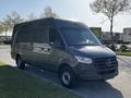 A 2021 Mercedes-Benz Sprinter van in dark gray parked with a sleek design and prominent front grille featuring the Mercedes-Benz logo