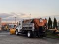 A 2006 Freightliner M2 106 snowplow truck with an orange plow attached at the front and a gray cargo box on the back