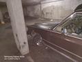 A 1982 Mercury Grand Marquis with dark brown paint and chrome accents partially obstructed by a concrete pillar