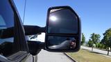 A 2017 Ford F-350 SD side mirror reflecting sunlight and the surrounding area with a visible silhouette of a person in the reflection