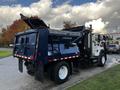 A blue 2011 International 7300 dump truck with a raised bed and side panel doors opened is parked in a lot