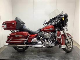 A 2010 Harley-Davidson FLHTCU motorcycle in a deep red finish with chrome accents and a large windshield, featuring saddlebags and a comfortable seat for touring